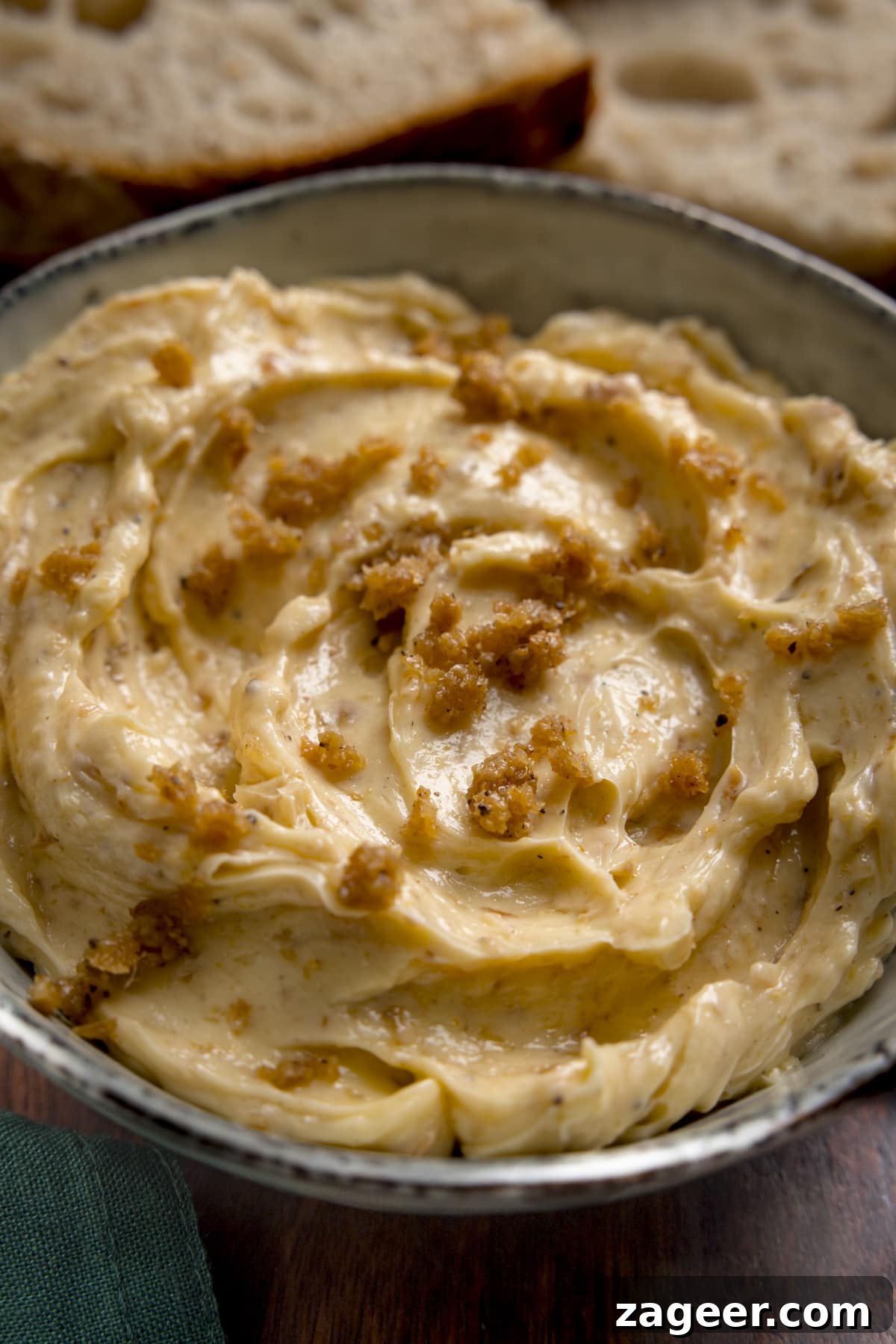 Crispy Chicken Skin Cracklings with Savory Butter Dip 13 Tall close up image of chicken skin butter in a bowl. There are slices of bread in the background.