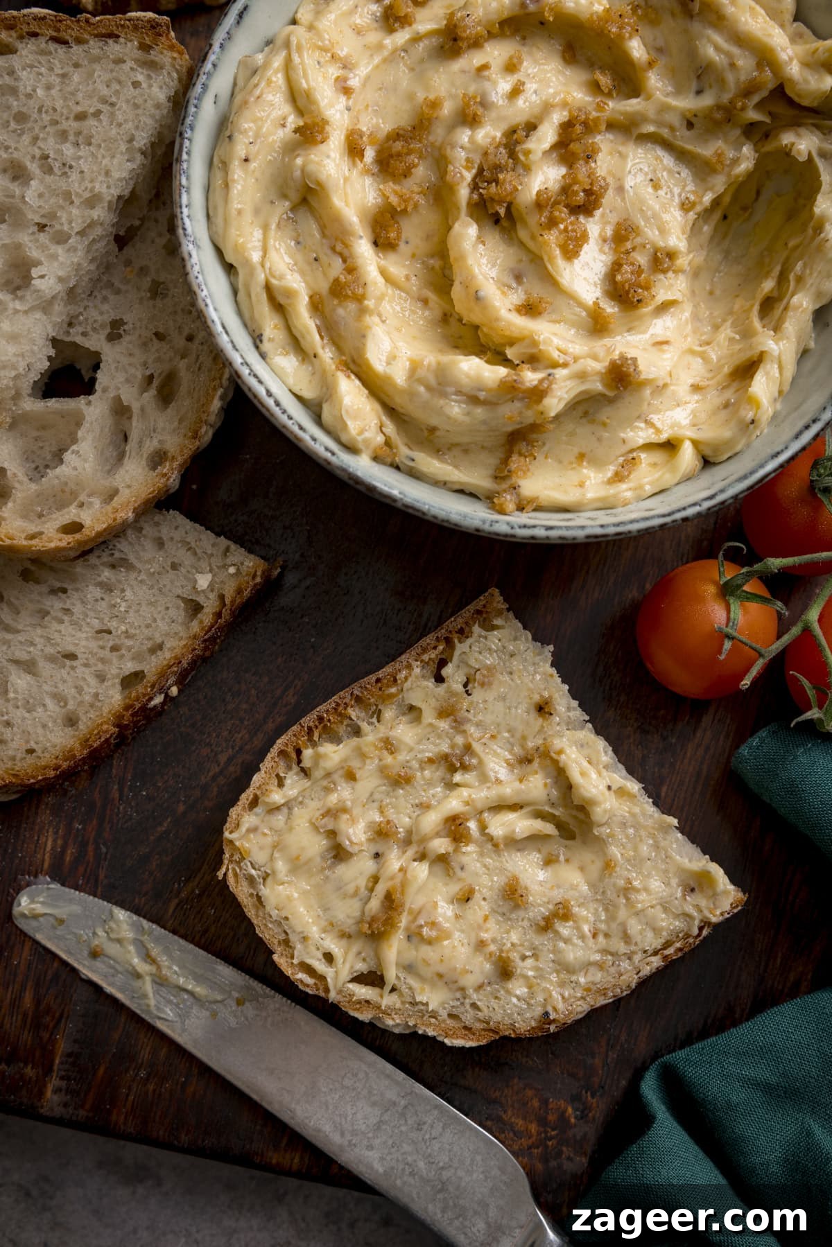 Crispy Chicken Skin Cracklings with Savory Butter Dip 5 A bowl of chicken skin butter and a piece of bread with the butter spread on it. There is also a knife, a couple of cherry tomatoes and sliced of un-buttered bread scattered around.