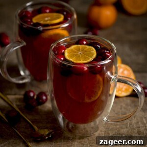 Homemade Mulled Cider Recipe for Cozy Fall Nights 10 Square image of 2 glass mugs filled with mulled cider. There are clementine slices and cranberries in the cider and the mugs are on a wooden table.