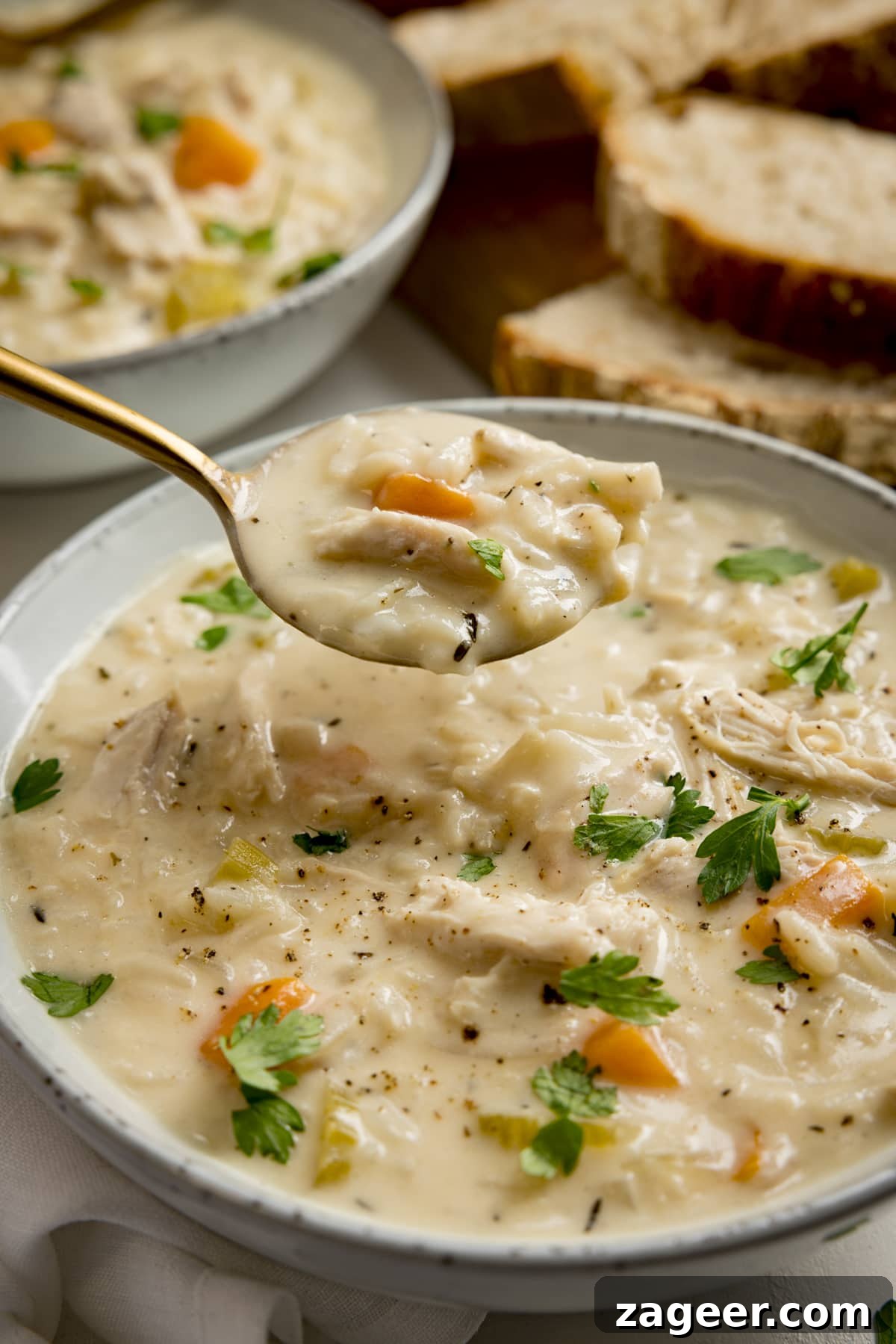 Classic Chicken and Rice Soup Recipe for Comforting Weeknight Meals 5 A spoonful being taken from a bowl of chicken and rice soup. There is a further bowl of soup and some bread slices in the background.