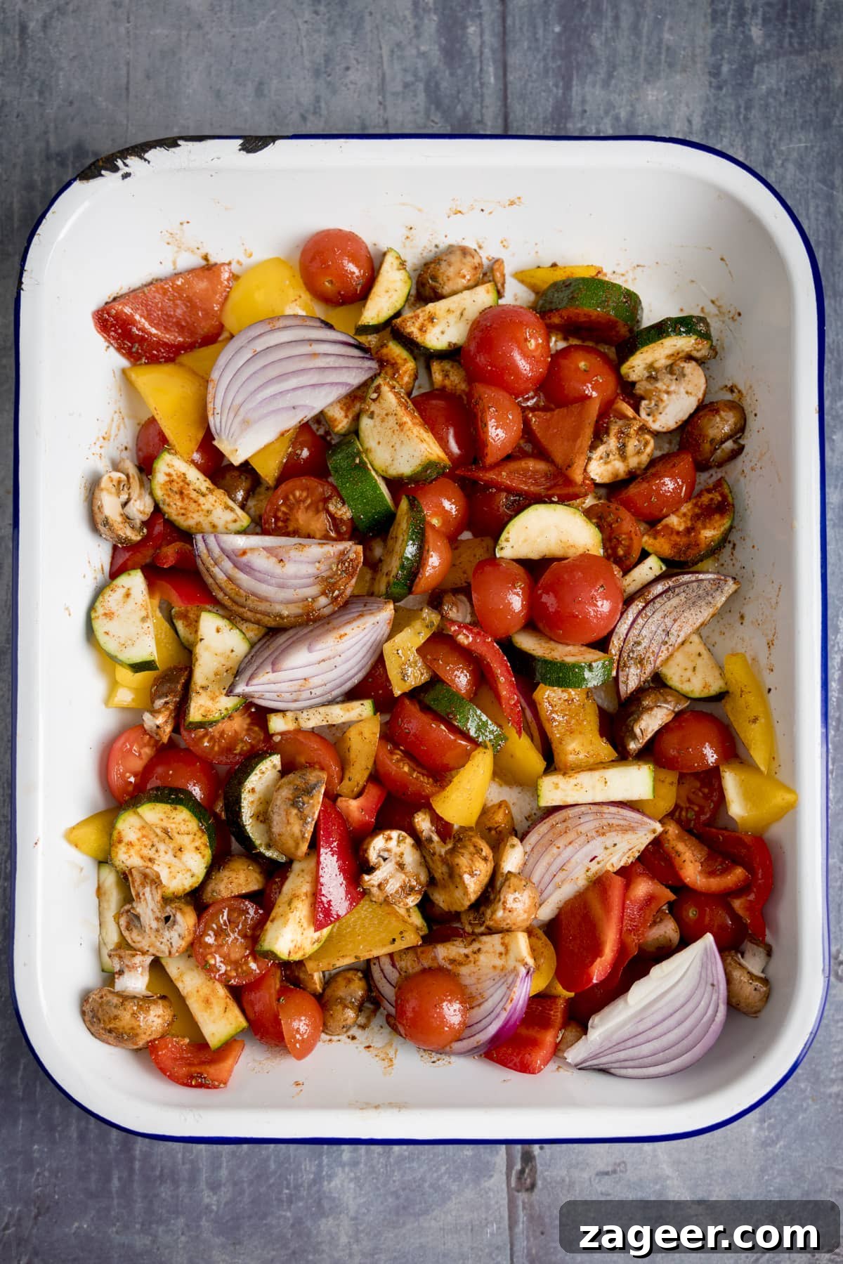 Roasted Veggie Pasta with Garlic and Parmesan 5 Overhead of a white tray filling with chopped vegetables on a blue background.