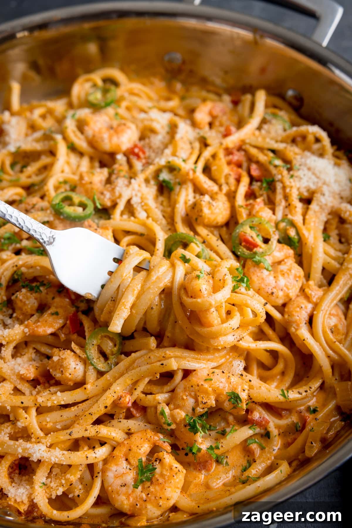 Creamy Cajun Shrimp Pasta Recipe — Quick Spicy Dinner 6 Tall image of a pan of prawn linguine in a creamy buffalo sauce. There is a fork taking some of the pasta from the pan.