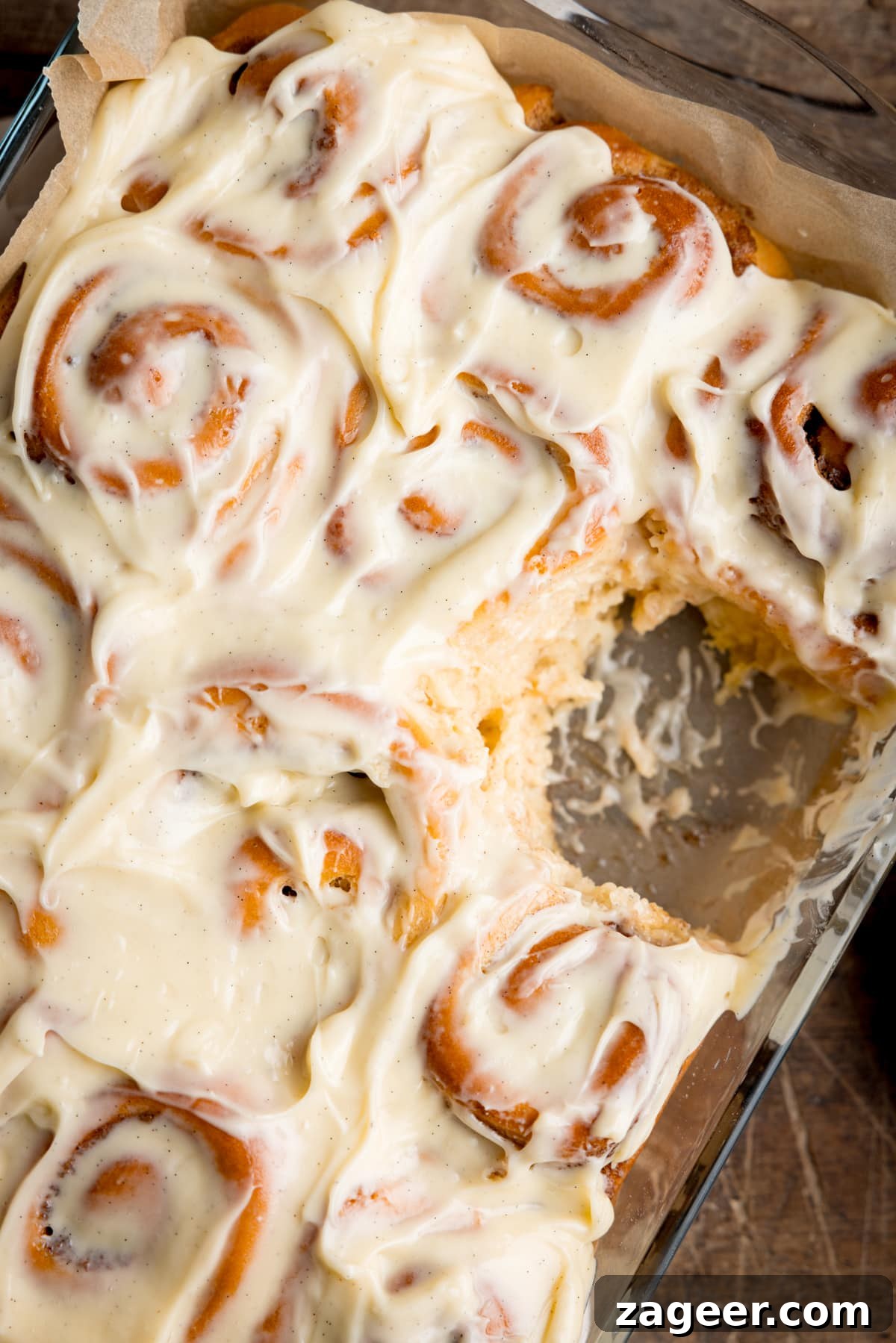 Fluffy Cinnamon Rolls Recipe for Soft, Homemade Swirls 2 Overhead image of a baking dish filled with cinnamon rolls, topped with cream cheese frosting. One cinnamon roll has been removed.