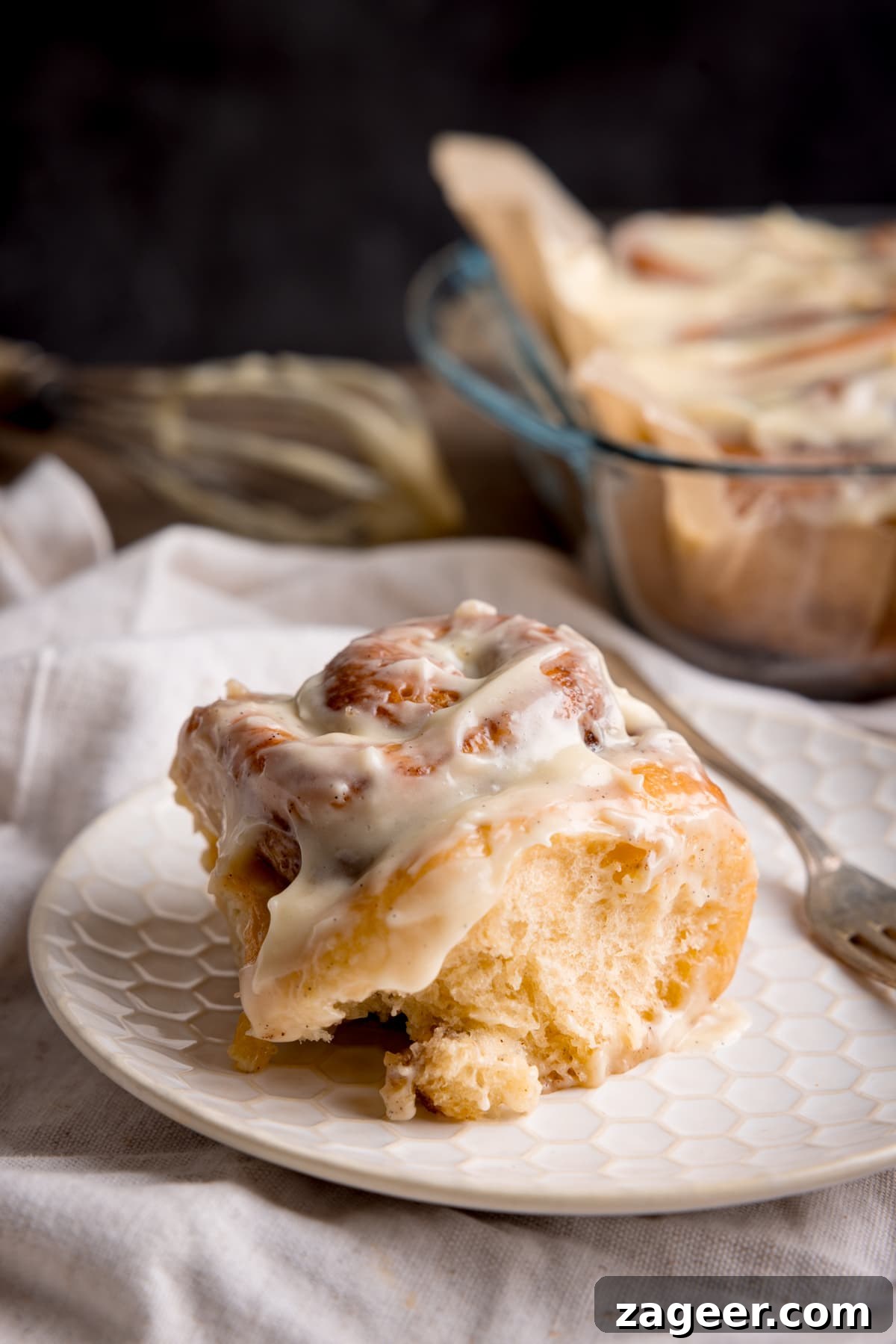 Fluffy Cinnamon Rolls Recipe for Soft, Homemade Swirls 10 A single frosted cinnamon roll on a white plate with a small fork next to it.