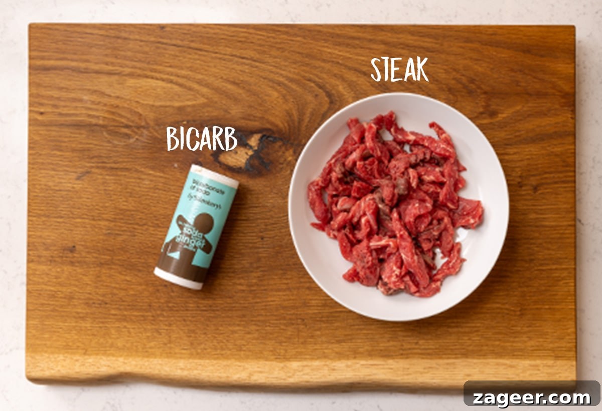 Stir-Fried Beef in Savory Black Bean Sauce Recipe 6 A white bowl filled with steak strips and a tub of bicarbonate of soda on a wooden board.