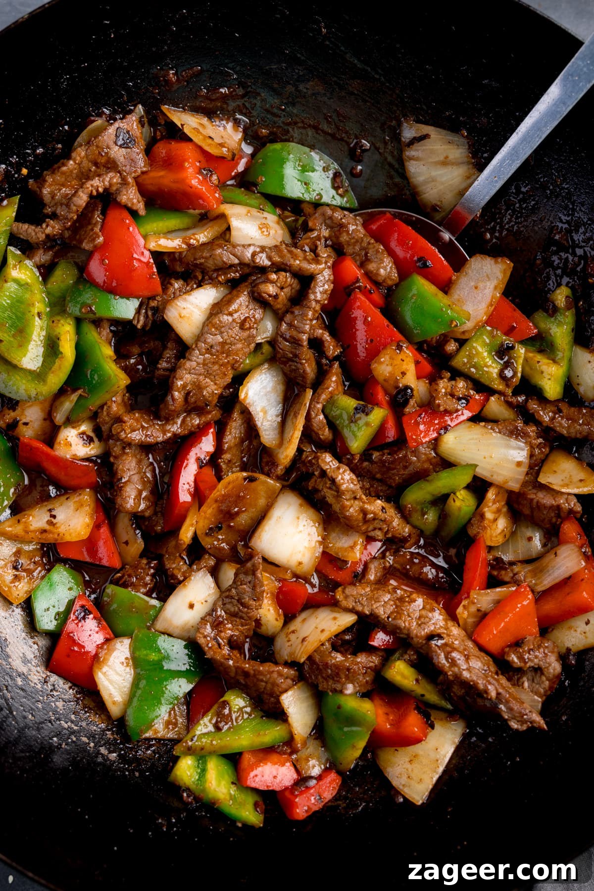 Stir-Fried Beef in Savory Black Bean Sauce Recipe 8 Close up overhead shot of beef in black bean sauce stir fry, with peppers and onions, in a wok, with a spatula sticking out.