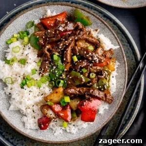 Stir-Fried Beef in Savory Black Bean Sauce Recipe 10 Beef in black bean sauce stir fry with boiled rice in a bowl, topped with spring onions and sesame seeds. There is a pair of black chopsticks next to the bowl.