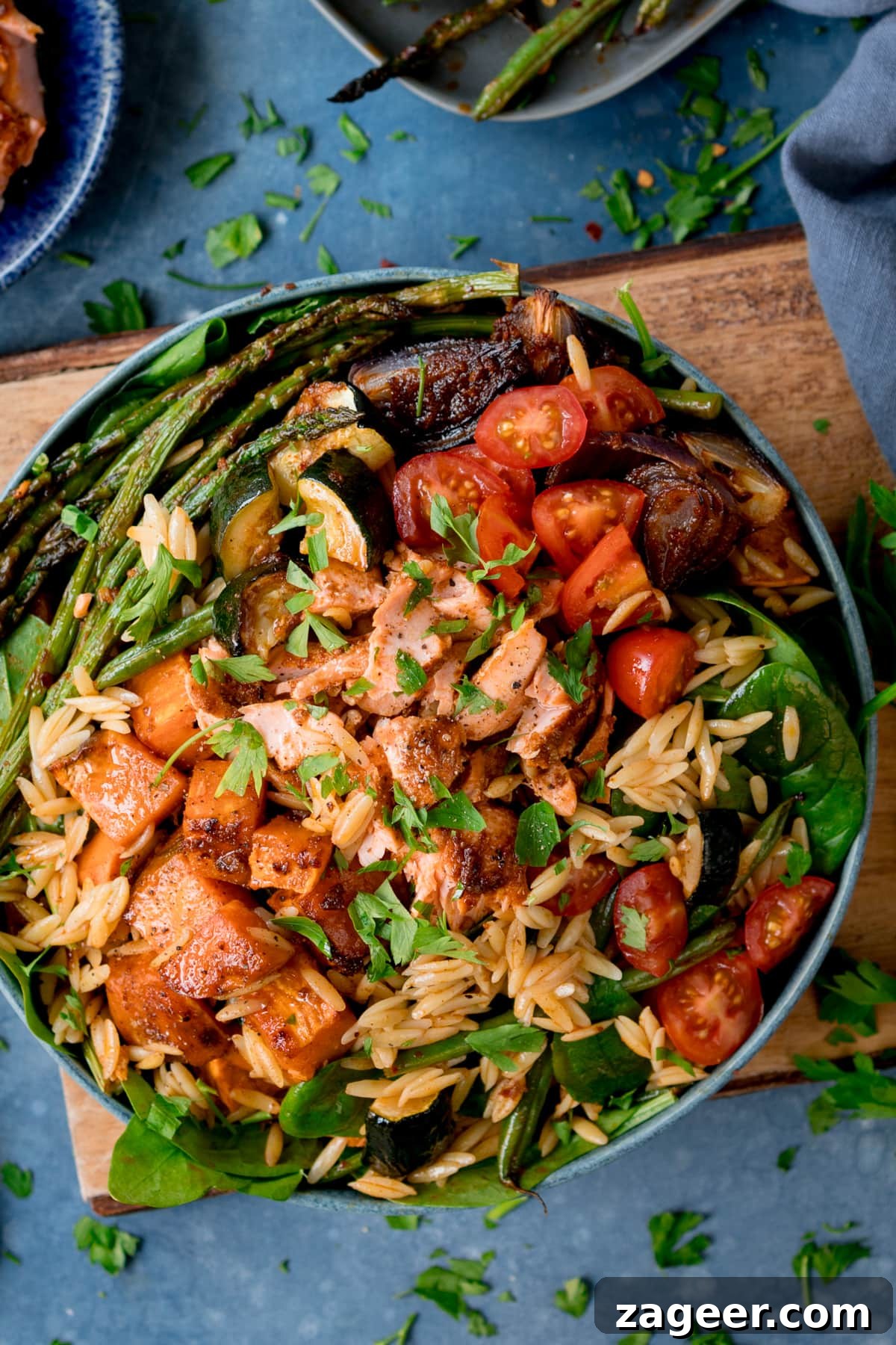 Lemon-Dill Salmon Orzo Pasta Salad for Weeknight Meals 2 A bowl full of orzo pasta salad with salmon and roasted vegetables on a wooden board with a blue background.