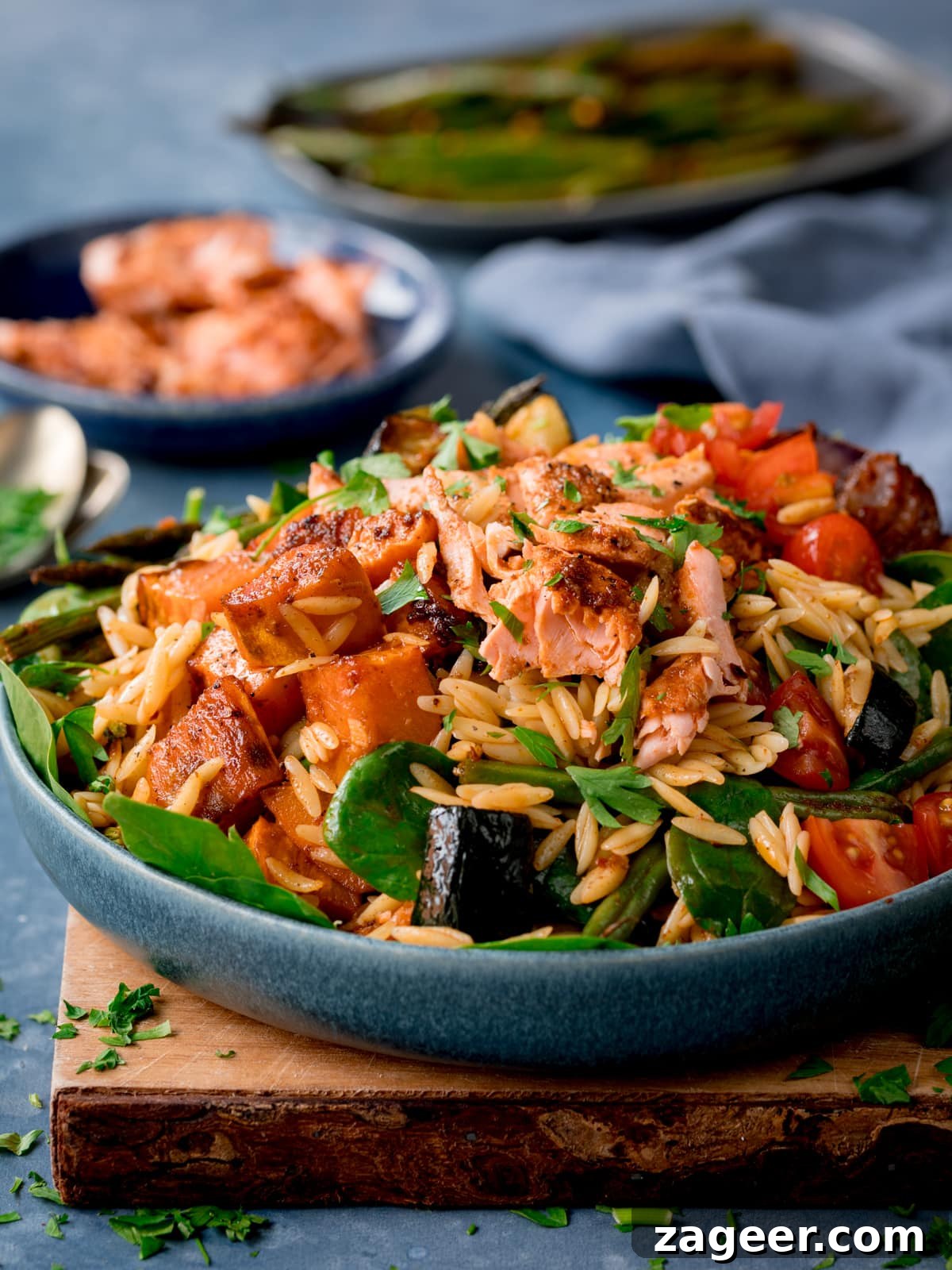 Lemon-Dill Salmon Orzo Pasta Salad for Weeknight Meals 5 Side photo of orzo pasta salad with salmon in a blue bowl sat on a wooden board.