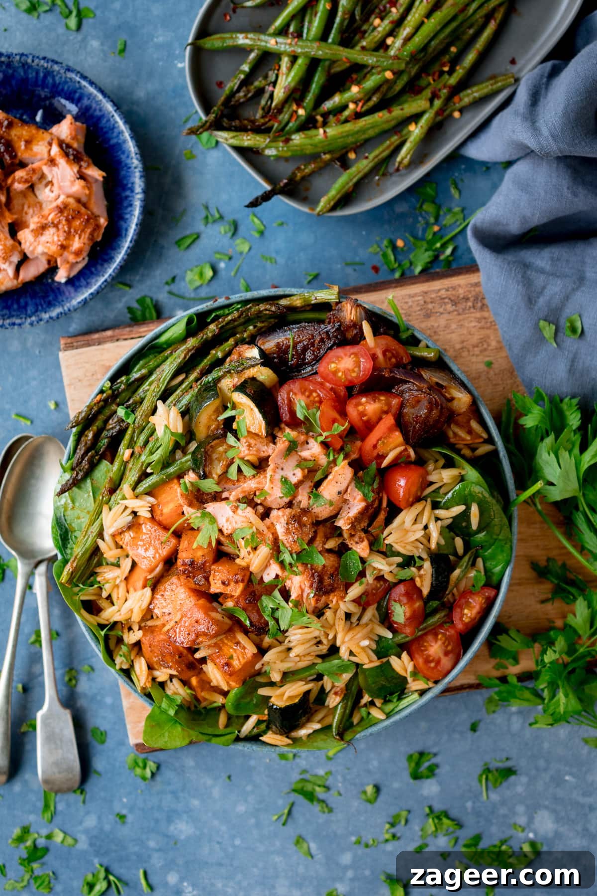 Lemon-Dill Salmon Orzo Pasta Salad for Weeknight Meals 6 A bowl full of orzo pasta salad with salmon and roasted vegetables on a wooden board with a blue background.