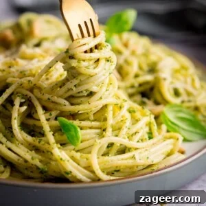 Creamy Basil Pesto Pasta with Garlic and Parmesan 6 Square image of pesto spaghetti on a light grey plate being swirled with a gold fork. The pasta is sprinkled with baby basil leaves, toasted pine nuts and parmesan. The plate is on a light grey surface.
