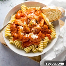 Chicken Paprikash in a white bowl on top of pasta with a piece of bread in the bowl.