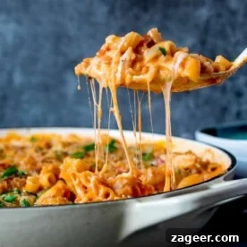 Square image of a spoonful of chicken and bacon mac and cheese being scooped out of pan. Cheese is stretching.