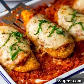 Baked breaded chicken parmesan fillets topped with melted cheese and fresh basil, served over a rich tomato sauce in a white dish.