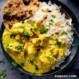 Chicken pasanda and rice on a dark plate with a piece of chapati on the plate.