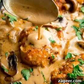 A spoon pours creamy Chicken Marsala sauce over browned chicken fillets, garnished with chopped parsley.