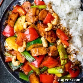 A plate of kung pao chicken with red peppers, courgette, spring onions, cashews, and white rice.