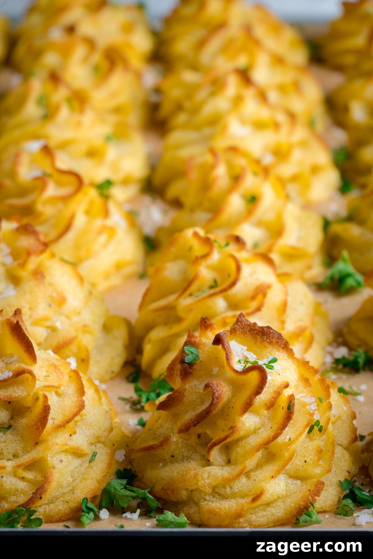 Creamy Duchess Potatoes Recipe for Perfect Sides 2 Close up image of a tray full of piped, baked, Duchess potatoes. The tray is lined with baking parchment. The potatoes are scattered with salt and parsley.