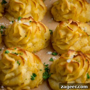Creamy Duchess Potatoes Recipe for Perfect Sides 11 Close up square image of a tray full of piped, baked, Duchess potatoes. The tray is lined with baking parchment. The potatoes are scattered with salt and parsley.