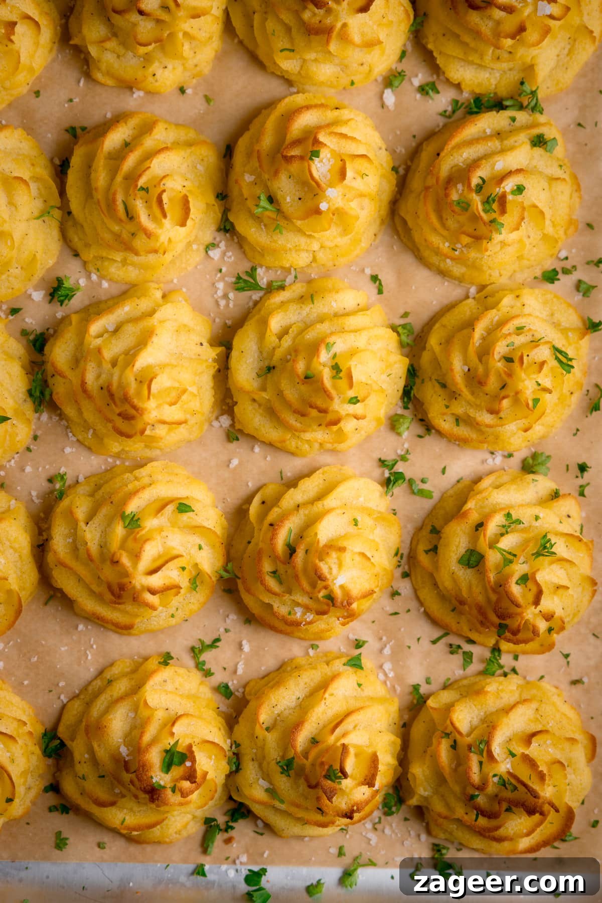 Creamy Duchess Potatoes Recipe for Perfect Sides 3 Overhead image of a tray full of piped, baked, Duchess potatoes. The tray is lined with baking parchment. The potatoes are scattered with salt and parsley.