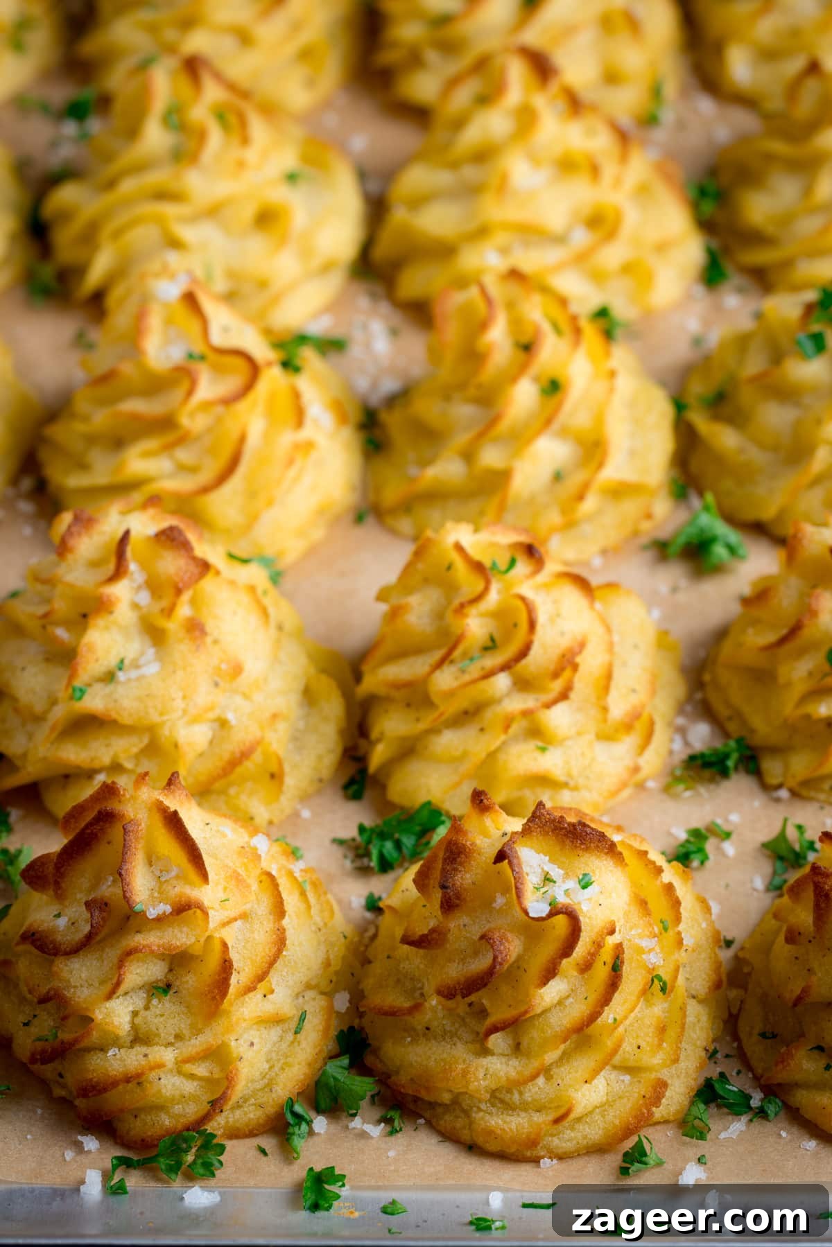 Creamy Duchess Potatoes Recipe for Perfect Sides 4 A tray full of piped, baked, Duchess potatoes. The tray is lined with baking parchment. The potatoes are scattered with salt and parsley.