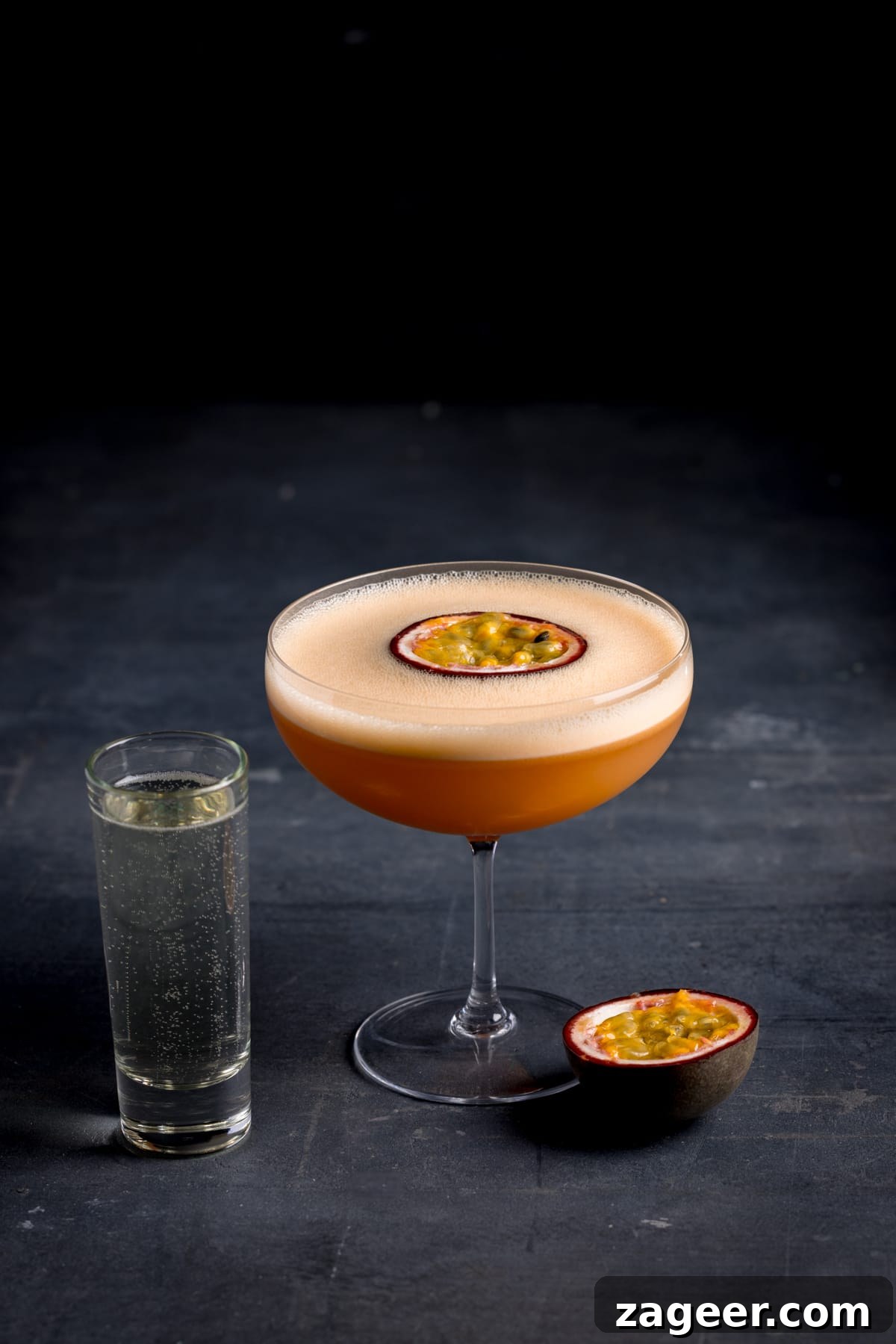 Pornstar Martini Cocktail Recipe with Passion Fruit and Prosecco 2 A glass of pornstar martini with a tall shot glass full of prosecco and half a sliced passion fruit next to it.