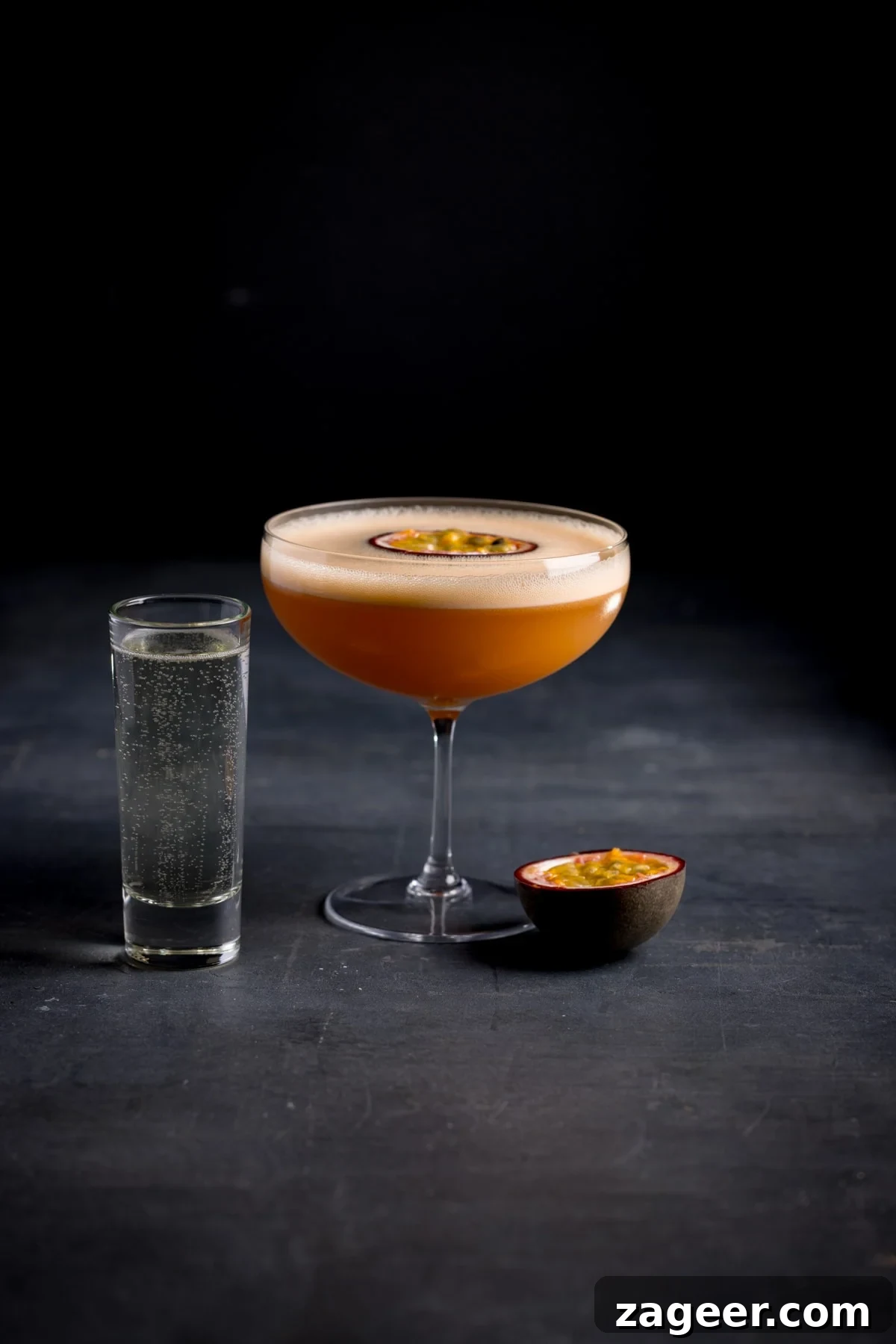 Pornstar Martini Cocktail Recipe with Passion Fruit and Prosecco 4 A glass of pornstar martini with a tall shot glass full of prosecco and half a sliced passion fruit next to it.