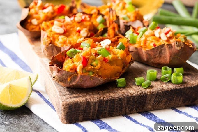 Crispy Thai-Style Sweet Potato Skins with Spicy Peanut Dip 4 Thai inspired sweet potato skins on a wooden board on top of a striped tea towel. The potato skins are topped with spring onions, chillies and peanuts. There are additional ingredients scattered around.