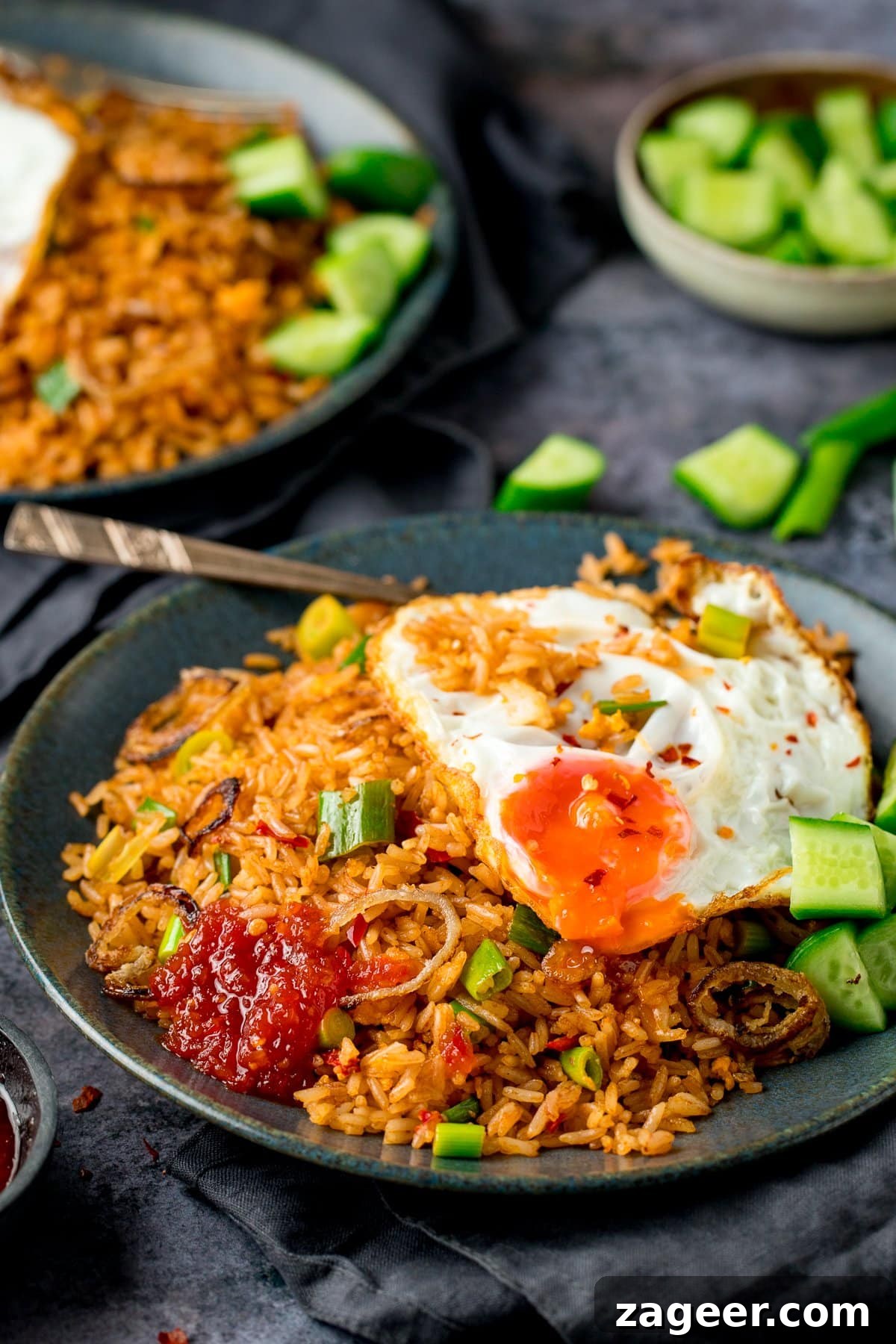 Nasi Goreng: Authentic Indonesian Fried Rice Recipe & Tips 2 nasi goreng rice on a plate, with a fried egg, chilli sauce and cucumber