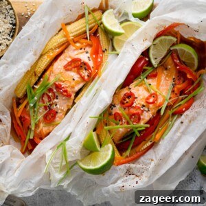 Salmon en Papillote: Steamed Baked Salmon Wrapped in Parchment 12 Square image of two salmon fillets cooked in individual baking parchment parcels with slices of chilli, peppers, babycorn, carrot and spring onion. Also topped with wedges of lime. The parcels are open, on a wooden board on a light background. There is a dish of sesame seeds nearby.