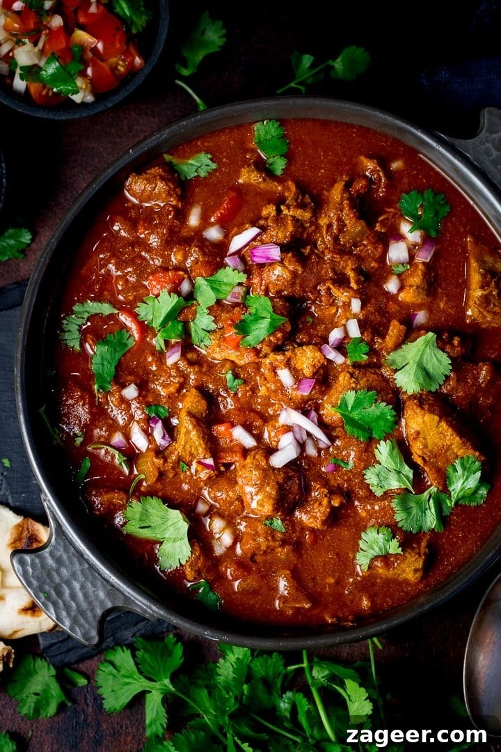 Low-Fat Slow-Cooked Spicy Beef Curry Recipe 2 Overhead image of beef curry in a dark dish topped with coriander, chillies and red onion