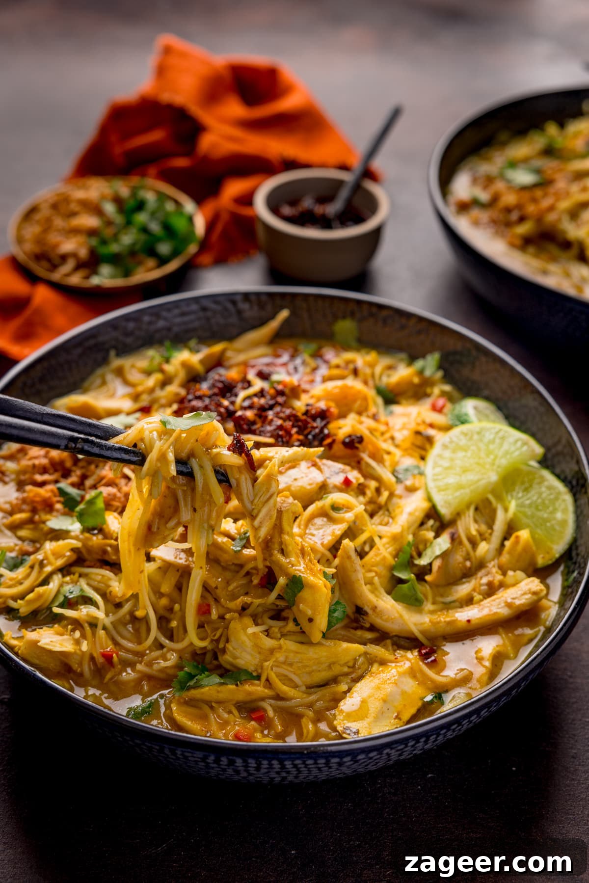 30-Minute Chicken Laksa Recipe: Flavorful Coconut Noodle Soup 7 Close up picture of some black chopsticks picking up some chicken and noodles from a bowl full of chicken laksa soup.