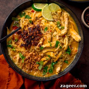 30-Minute Chicken Laksa Recipe: Flavorful Coconut Noodle Soup 8 Overhead picture of a black textured bowl full of chicken laksa topped with chilli crisp and coriander.