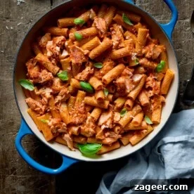 Square image of rigatoni and salmon in creamy tomato sauce in a blue cast iron pan on a wooden table.
