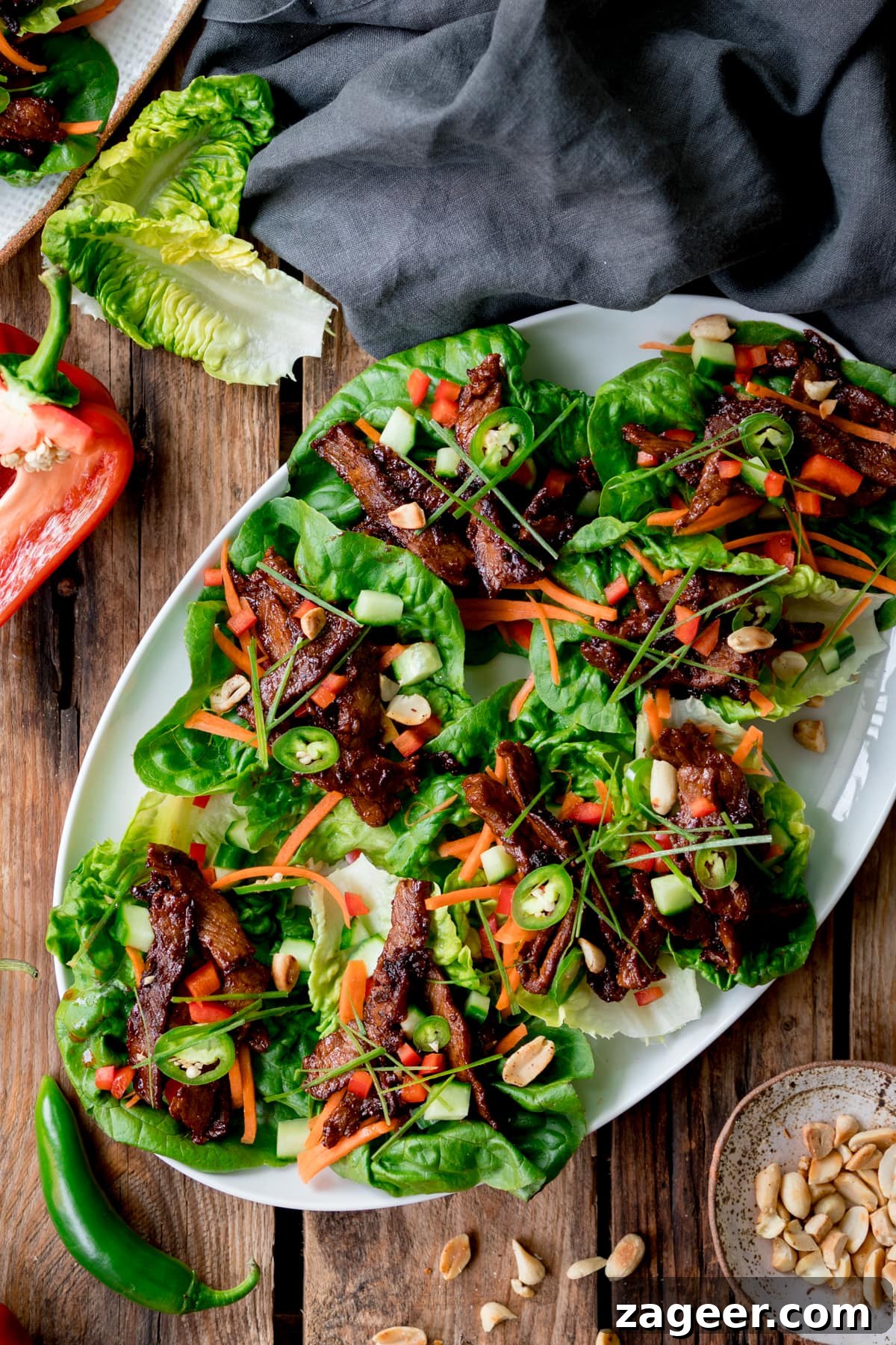 Overhead picture of a white plate full of Korean lettuce wraps all sat on a rustic wooden board with some peanuts and chillis in the background.