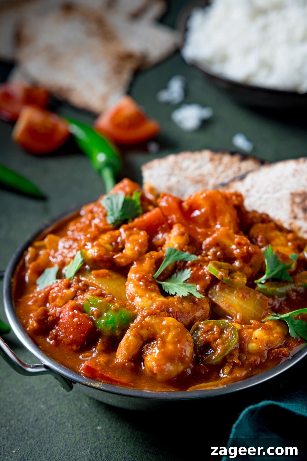 Prawn Balti Curry Recipe: Flavorful Indian-Style Shrimp Curry 4 Picture of a prawn curry in a balti dish with a bowl of boiled rice and some chapati in the background.