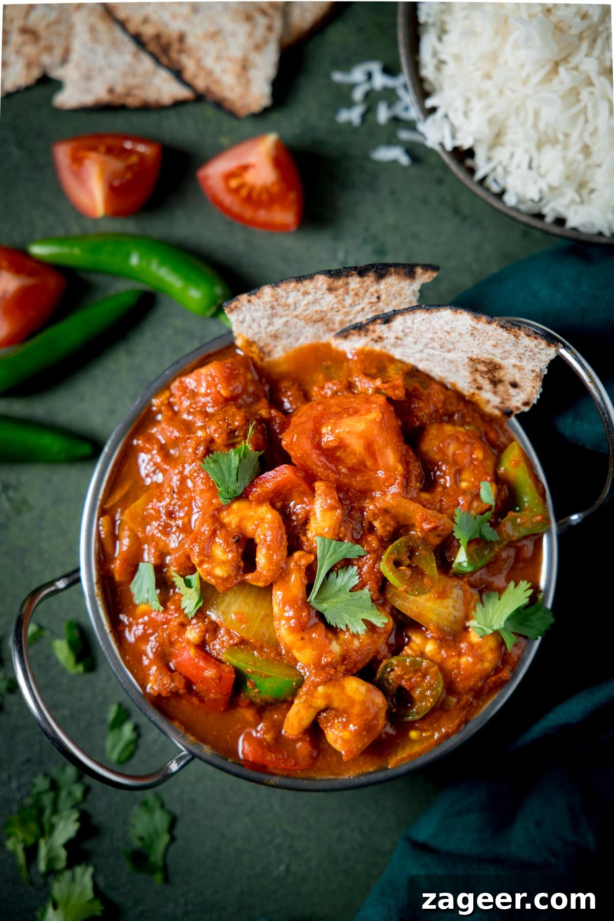 Prawn Balti Curry Recipe: Flavorful Indian-Style Shrimp Curry 5 Overhead picture of a prawn balti in a silver balti dish on a green background with some rice and toasted chapati in the background.