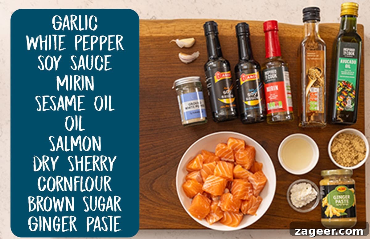 Crispy Air Fryer Teriyaki Salmon Recipe in 20 Minutes 3 An overhead shot of the ingredients of Air Fryer Teriyaki Salmon laid out on a wooden cutting board, which is on a white surface. To the left of the ingredients is a teal rectangle with the ingredient names written in white. They are as follows: garlic, white pepper, soy sauce, mirin, sesame oil, oil, salmon, dry sherry, cornflour, brown sugar, and ginger paste.