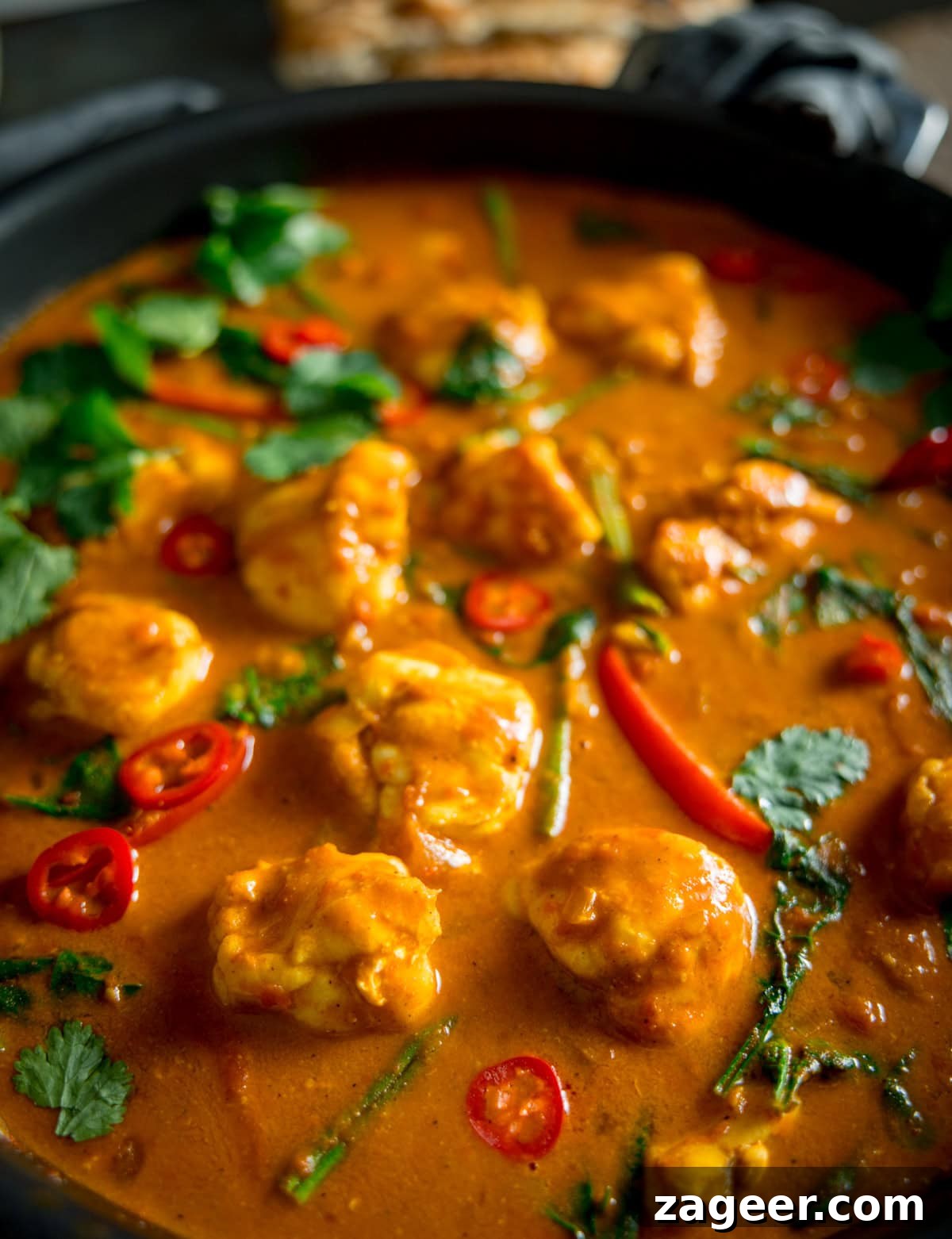 Creamy Monkfish Coconut Curry Recipe for Flavorful Dinner 4 A closeup shot of Monkfish Coconut Curry in a grey pan, topped with coriander. On a grey surface with a grey napkin in the background.