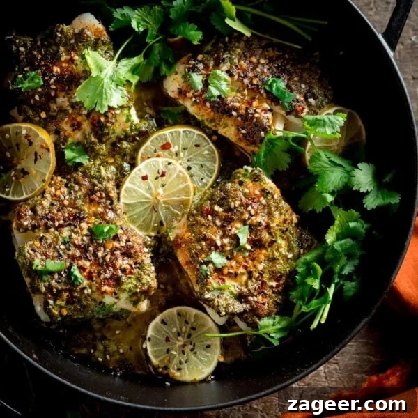 Creamy Monkfish Coconut Curry Recipe for Flavorful Dinner 7 A square photo of a big pan of coriander lime cod bake, garnished with slices of lime and coriander stalks, on a table with an orange napkin to the side.