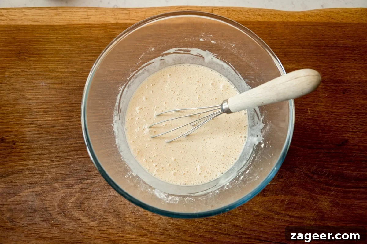 Crispy Beer-Battered Fish Recipe for Perfect Fried Fish 4 A wide, overhead shot of the finished beer batter. The batter is in a clear, glass bowl with a whisk wooden handle in the batter. All this is laid on a wooden board.