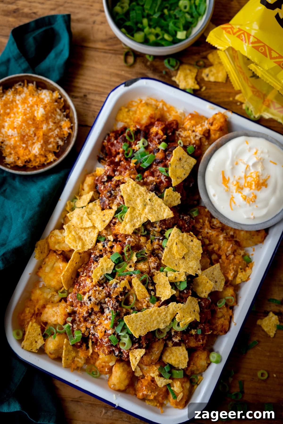 Loaded Totchos: Crispy Hash Brown Bites with Cheesy Toppings 5 A tall image of loaded Tochos, topped with crumbled tortilla chips, grated cheese and spring onions