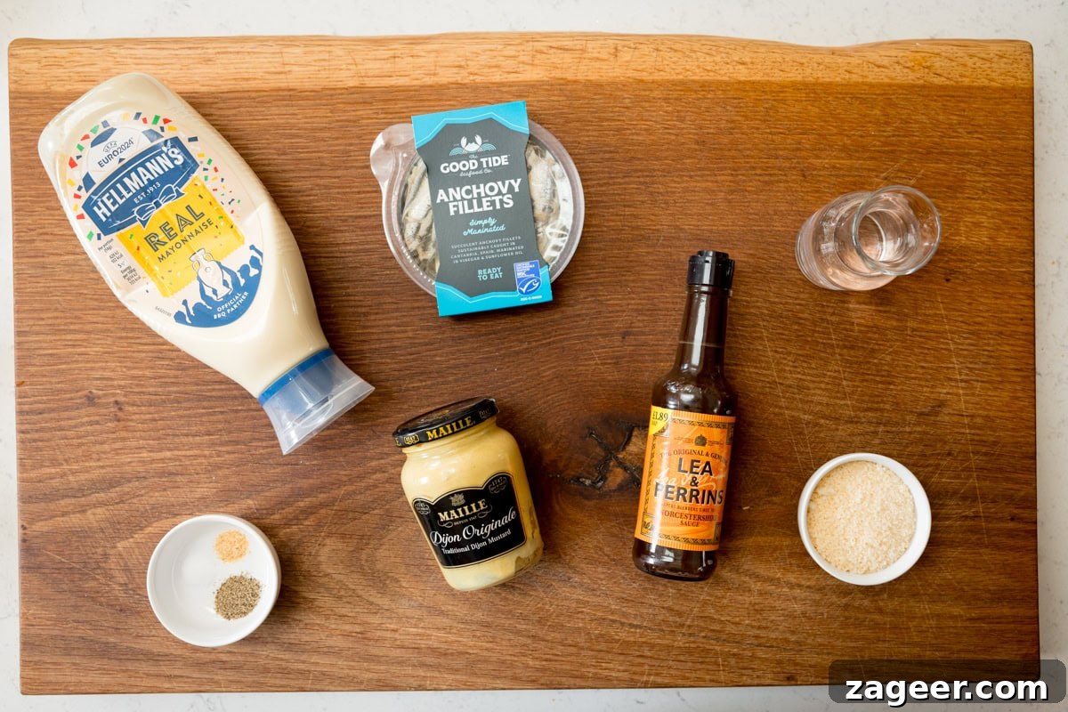 Authentic Caesar Salad Dressing Recipe You Can Make at Home 3 A wide overhead shot of the ingredients for Caesar Dressing. They are laid out on a wooden board. The ingredients are as follows: anchovies, mayonnaise, mustard, Worcestershire sauce, grated parmesan, pepper, salt, garlic powder, and water.