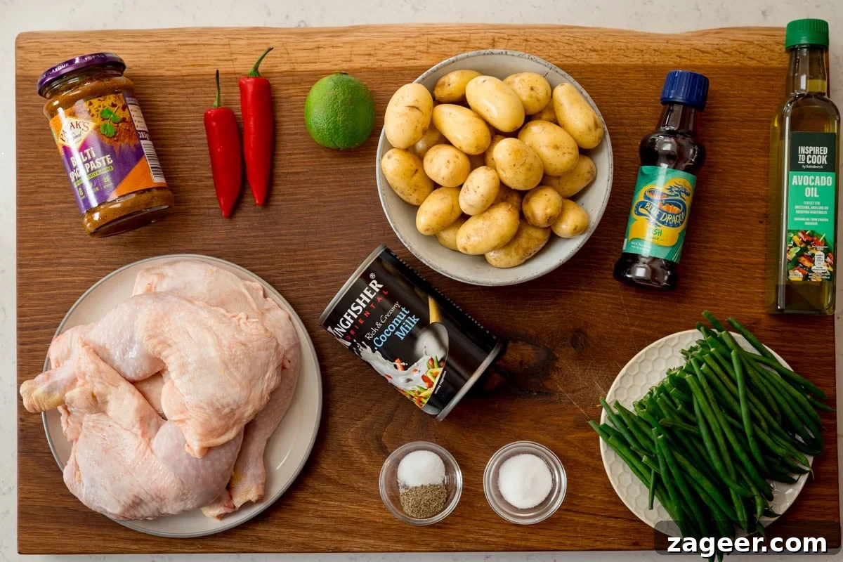 Comforting Chicken and Potato Curry Recipe for Weeknight Dinners 3 A wide, overhead shot of the ingredients for Chicken and Potato Curry. The ingredients are laid out on a wooden board, which is on top of a white marble surface. They are as follows: Chicken, Curry Paste, Oil, Salt, Pepper, Baby New Potatoes, Lime, Coconut Milk, Fish Sauce, Sugar, Green Beans, and Red Chillis.