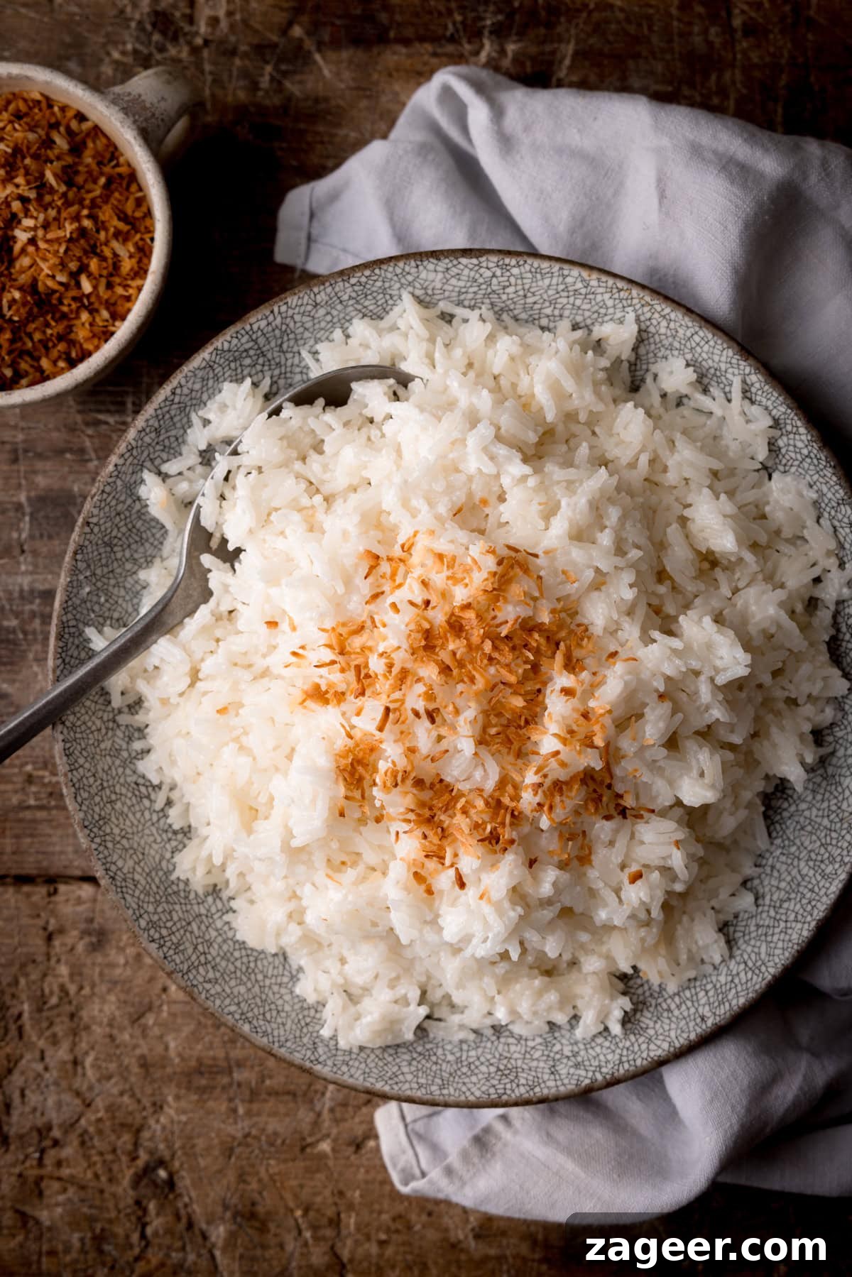 Stovetop Coconut Rice Recipe: Creamy, Fragrant Coconut Rice 5 Stovetop Coconut Rice on a light grey plate with a silver spoon and toasted shredded coconut in a mug.
