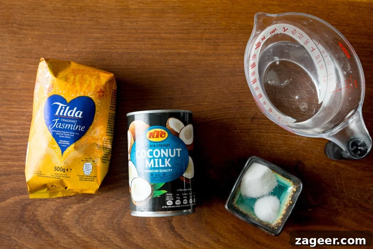 Perfect Coconut Rice in a Rice Cooker: Fluffy, Creamy Recipe 3 A wide, overhead shot of the ingredients for Rice Cooker Coconut Rice. The ingredients are laid out on a wooden board. They are as follows: Jasmine Rice, Coconut Milk, Sugar, Salt, and Water.