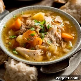 Chicken and vegetable soup served with a chunk of bread.
