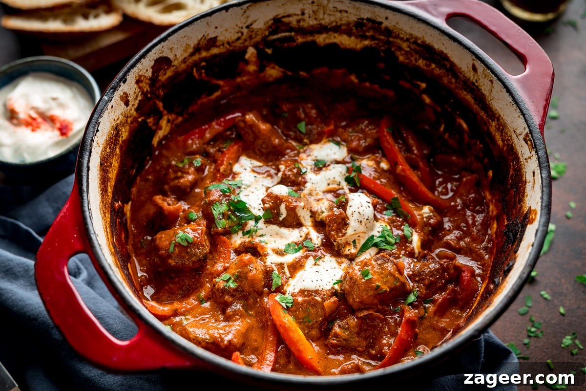 Authentic Hungarian Beef Goulash Recipe — Hearty Slow-Cooked Stew 7 wide image of Beef Goulash in a red casserole pan, topped with sour cream