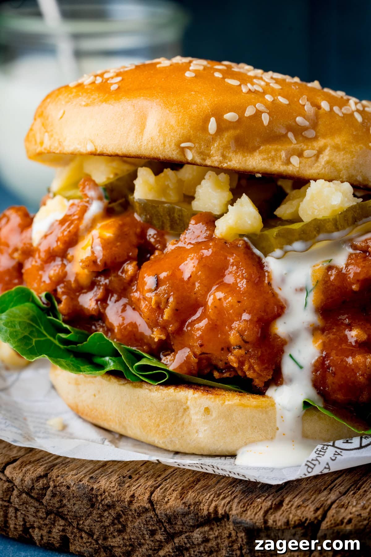A tall, closeup image of a Buffalo Chicken Burger on a cutting board with a jar of ranch in the background.