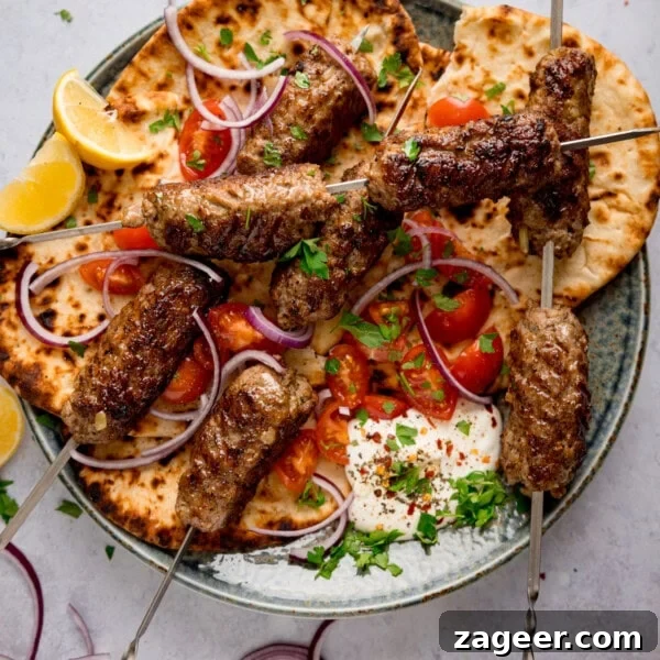 Grilled lamb kofta skewers on flatbread with sliced red onions, cherry tomatoes, lemon wedges, fresh herbs, and a dollop of whipped feta on a plate.